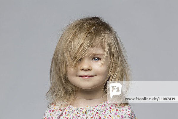 Porträt eines lächelnden Mädchens mit zerzaustem Haar vor grauem Hintergrund