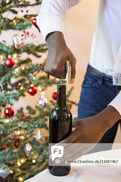 Mann öffnet eine Flasche Wein beim Weihnachtsessen