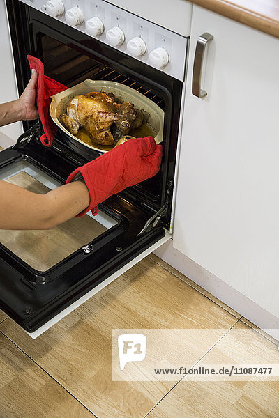Woman taking a roast chicken from the oven