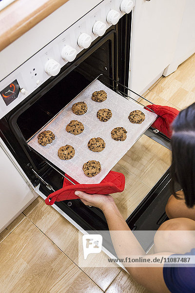 Frau nimmt frisch gebackene Kekse aus dem Ofen