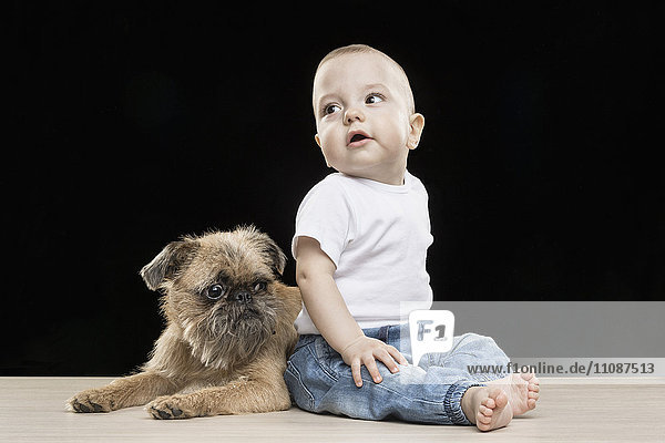 Süßer Junge sitzend mit Hund auf Tisch vor schwarzem Hintergrund