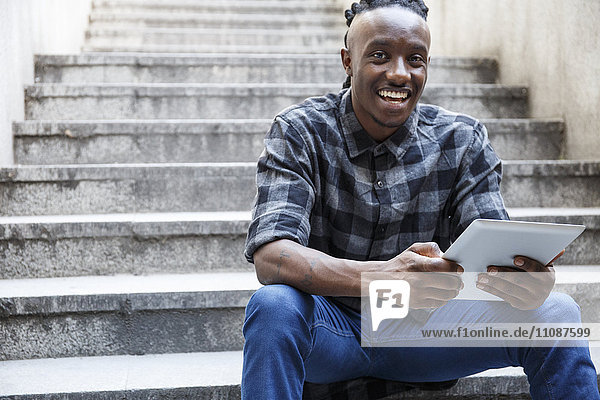 Junger Mann auf der Treppe sitzend  mit Hilfe eines digitalen Tabletts