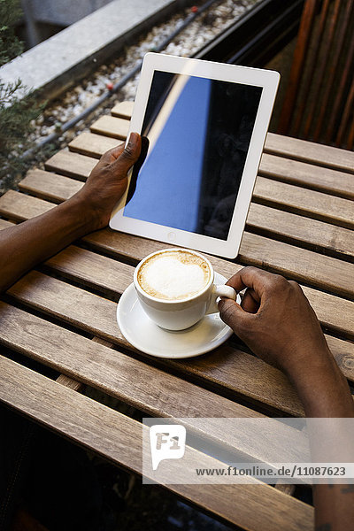Junger Mann sitzt im Cafe und benutzt ein digitales Tablett.