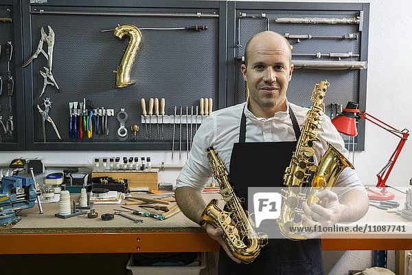 Portrait of an instrument maker holding two saxophones in his workshop