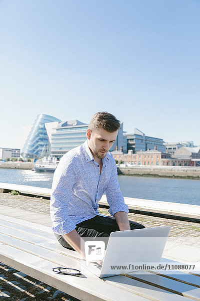 Irland  Dublin  junger Geschäftsmann auf der Bank sitzend mit Laptop