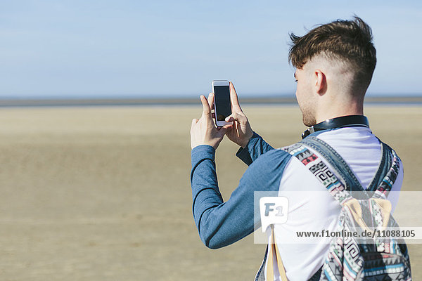 Young man taking picture with smartphone on the beach