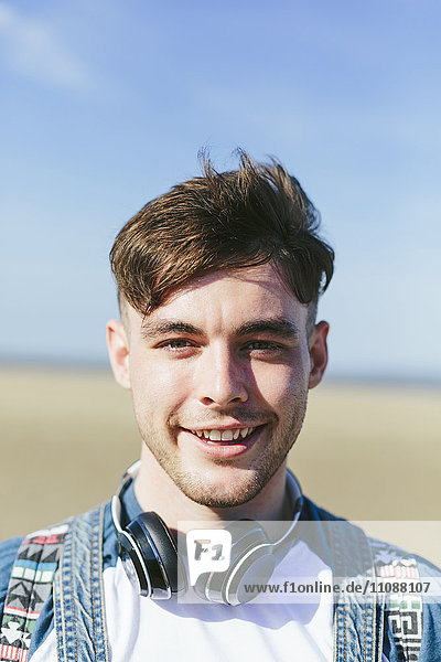Portrait of smiling young man with headphones on the beach