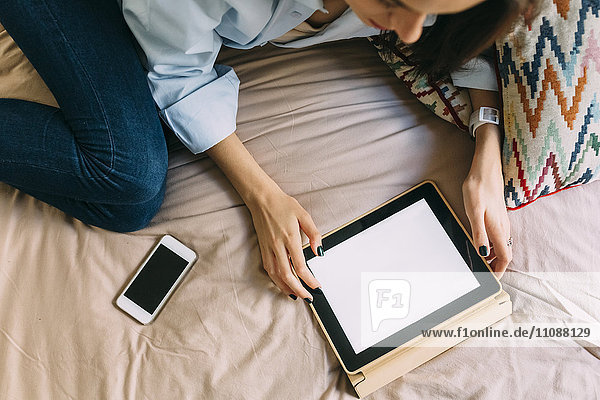 Junge Frau mit digitalem Tablett im Bett Smartphone
