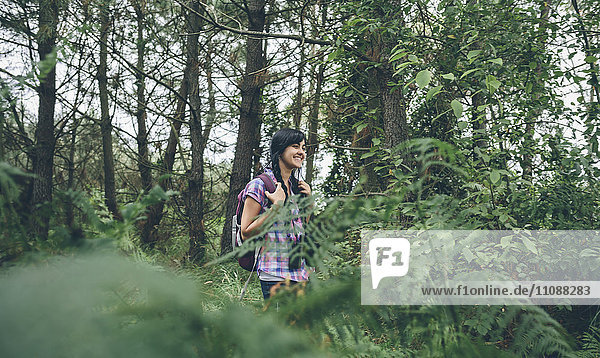 Smiling young woman with backpack walking in the forest