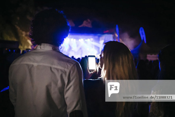 Rückansicht der jungen Frau beim Fotografieren mit dem Smartphone beim Sommerkonzert