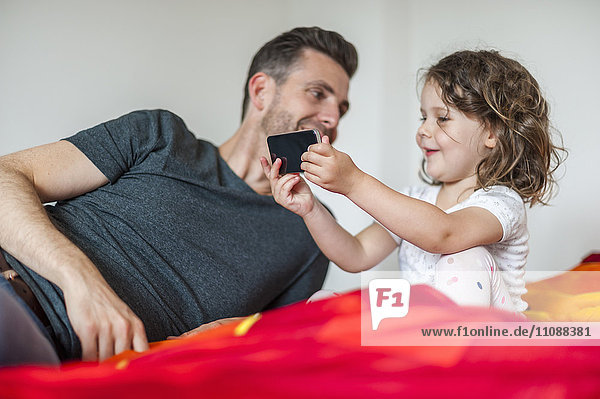 Vater und Tochter mit Handy im Bett