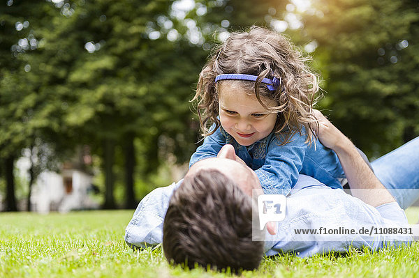 Vater kuschelt mit Tochter auf Wiese im Park