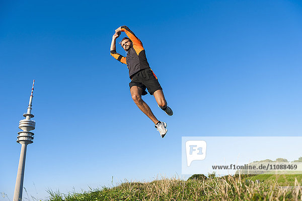 Sportler beim Springen auf der Wiese unter blauem Himmel