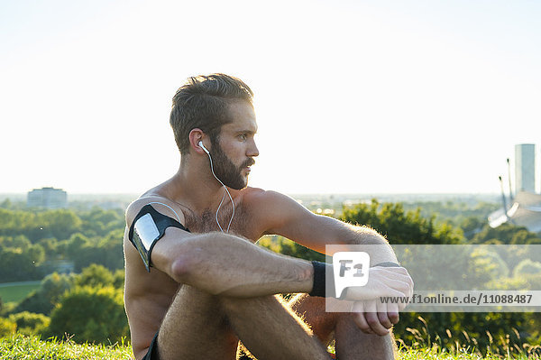 Athlete sitting on a meadow listening to music after workout