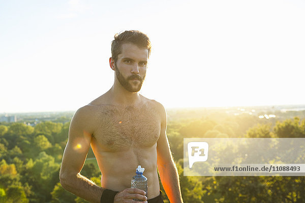 Barechested Athlet mit Wasserflasche bei Sonnenuntergang