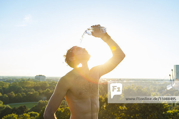 Barechested Athlet gießt Wasser über sein Gesicht bei Sonnenuntergang