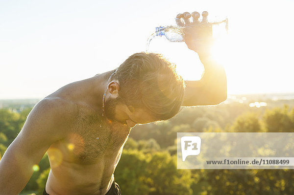 Barechested Athlet gießt Wasser über seinen Kopf bei Sonnenuntergang