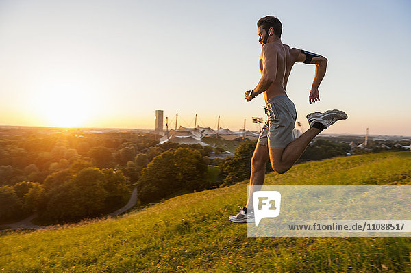Barechested man running on meadow in park at sunset