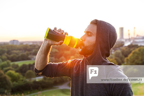 Sportler beim Trinken aus der Flasche bei Sonnenuntergang
