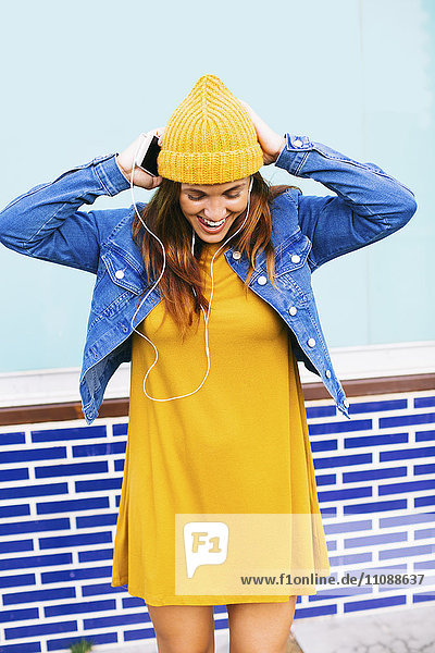 Junge Frau mit gelber Mütze und Kleid  Musik hören mit Kopfhörern