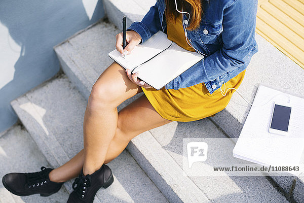 Junge Frau auf einer Treppe sitzend  etwas aufschreibend  Teilansicht