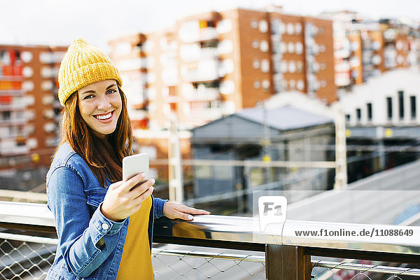 Porträt einer lächelnden jungen Frau mit gelber Mütze auf dem Handy
