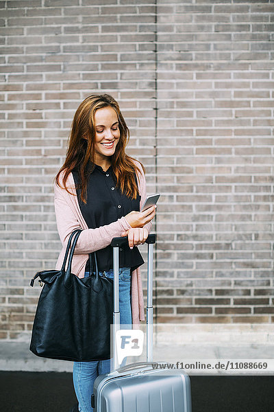 Lächelnde Frau mit Gepäck beim Blick aufs Handy