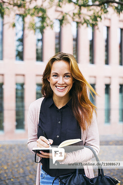 Porträt einer lächelnden jungen Frau mit Notizbuch