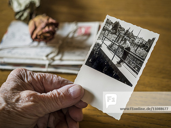 Alte Frau hält Bild ihrer Jugendfreundin in der Hand  alte Briefe und getrocknete Rose
