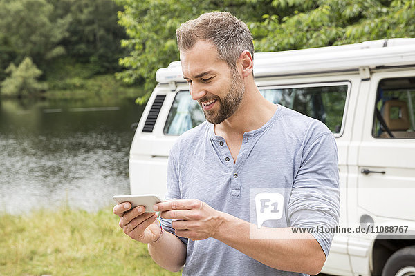 Mann mit Handy in einem Van am Seeufer