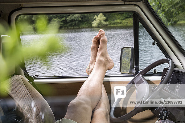 Die Beine eines Mannes  der sich in einem Van am Seeufer entspannt.