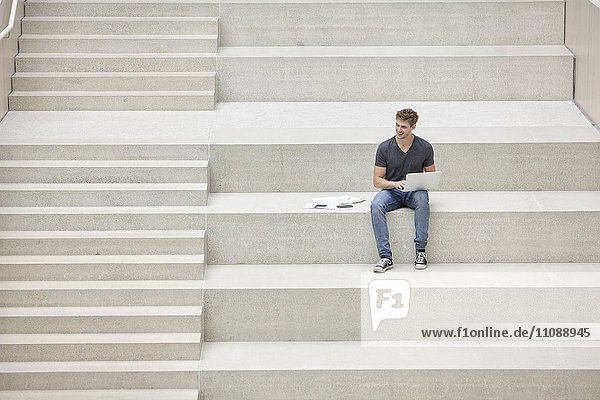 Junger Mann auf der Treppe sitzend mit Laptop