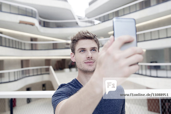 Junger Mann  der einen Selfie in einem modernen Bürogebäude nimmt.