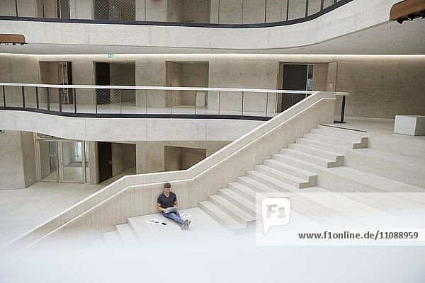Junger Mann sitzt auf der Treppe im Bürogebäude mit Laptop