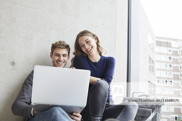 Smiling young couple sitting at concrete wall sharing laptop