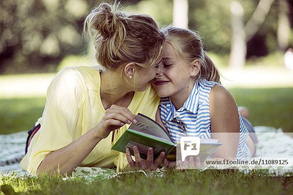 Fröhliches Mädchen und junge Frau mit Buch auf Decke im Park