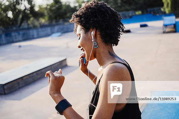 Lächelnde junge Frau mit Kopfhörern tanzend im Skatepark