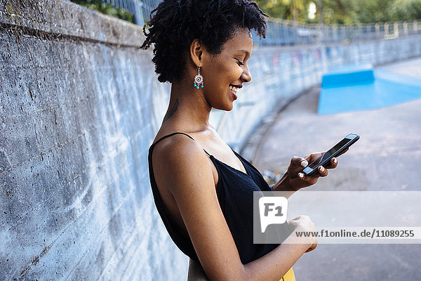 Lächelnde junge Frau im Skatepark mit Blick auf das Handy