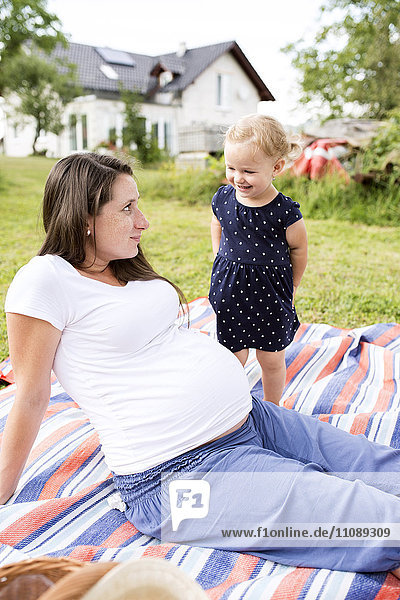 Schwangere Mutter sitzend auf Picknickdecke mit kleiner Tochter