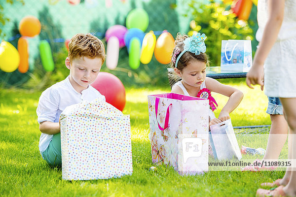Little boy and girl unpacking birthday presents in the garden