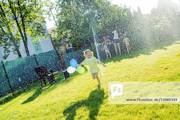 Little girl having fun with lawn sprinkler in the garden