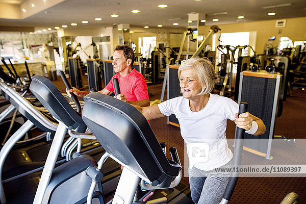 Senior man and mature woman on step machine in fitness gym