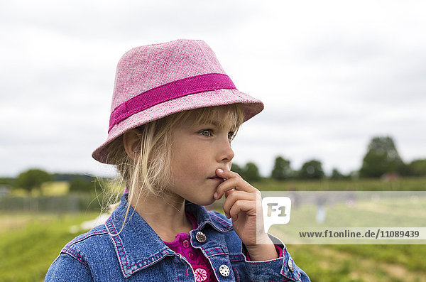 Porträt eines nachdenklichen kleinen Mädchens mit rosa Hut auf einem Erdbeerfeld