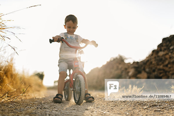 Kleiner Junge mit Kinderfahrrad auf Schotterpiste