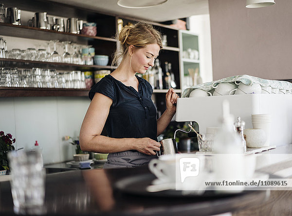Frau in einem Café bereitet Milchschaum für Kaffee zu