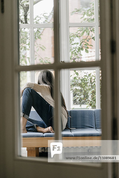Back view of woman sitting on lounge in winter garden looking through window