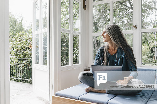 Frau mit Laptop auf der Lounge im Wintergarten mit Blick durch geöffnete Terrassentür
