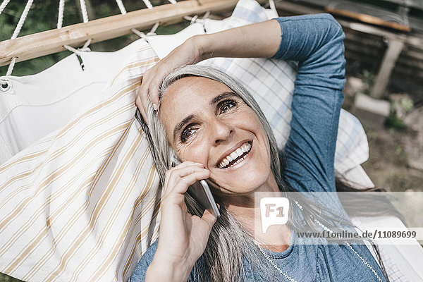 Porträt der lachenden Frau am Telefon in der Hängematte liegend