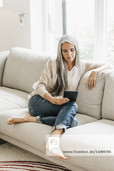 Frau mit langen grauen Haaren sitzt auf der Couch mit E-Book