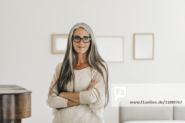 Porträt einer lächelnden Frau mit langen grauen Haaren und Brille zu Hause